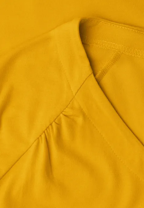 Geel shirt met V-hals en subtiele plooien bij de schouders.