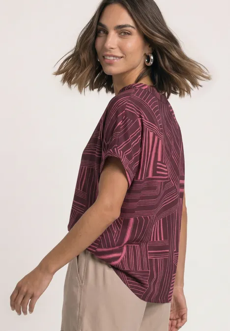 Une femme porte un haut rouge à motifs géométriques à manches courtes et un pantalon beige.
