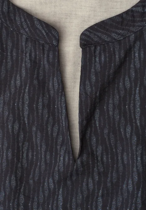Dunkles Shirt mit blauem Wellenmuster und V-förmigem Kragen auf hellem Stoffhintergrund.