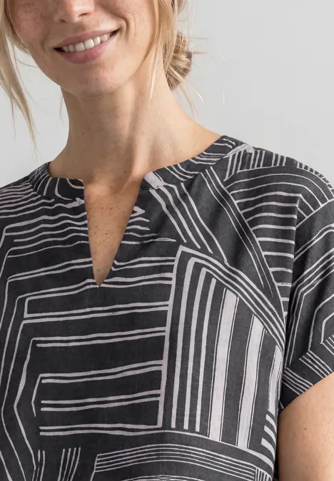 Frau im Schwarz-Weiß-Shirt mit geometrischem Linienmuster und leichtem Lächeln.
