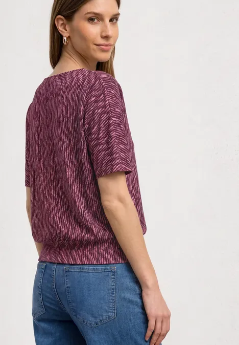 Shirt met boothals en elastische zoom blush berry Vrouw van achteren in een paarse gebreide top en blauwe spijkerbroek tegen een lichte achtergrond.