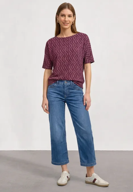 Shirt met boothals en elastische zoom blush berry Vrouw met een kort mouw shirt met patroon, brede cropped spijkerbroek en witte sneakers tegen neutrale achtergrond.