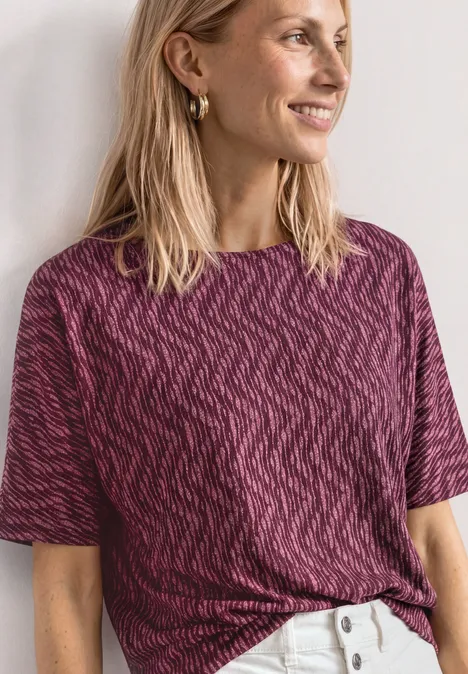 T-shirt à col bateau et ourlet élastiqué blush berry Eine Person trägt ein kurzärmeliges, dunkelpinkes, gemustertes Shirt und weiße Hosen.