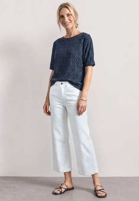 Shirt met boothals en elastische zoom ashen blue Vrouw met donkerblauw gestructureerd T-shirt, witte culottebroek en zwarte sandalen op neutrale achtergrond.