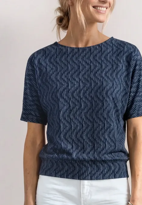 Shirt met boothals en elastische zoom ashen blue Vrouw in een blauwe top met zigzagpatroon en witte broek, glimlachend met haar in een knot.