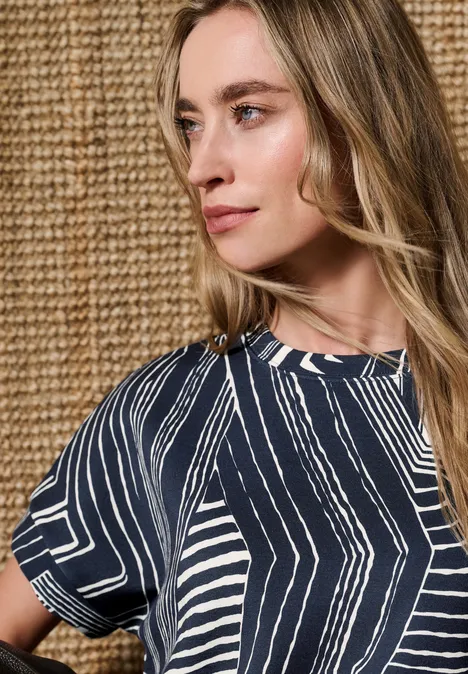 Vrouw met blauw-wit patroonshirt voor een beige gevlochten muur.