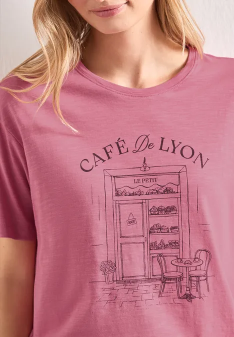 T-shirt rose avec façade dessinée du Café de Lyon, porte, table et chaise.
