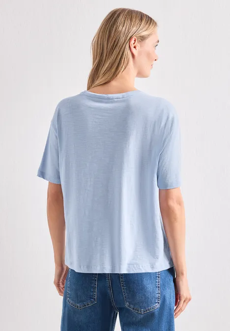 Vue arrière d'une femme portant un t-shirt bleu clair et un jean devant un fond blanc.