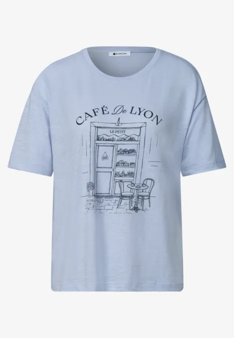 T-shirt bleu clair avec motif Café de Lyon dessiné, façade, table et chaises en esquisse noire.