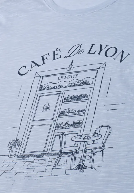 Dessin sur T-shirt: devanture du 'Café De Lyon' avec vitrine de pâtisseries, table et chaises.