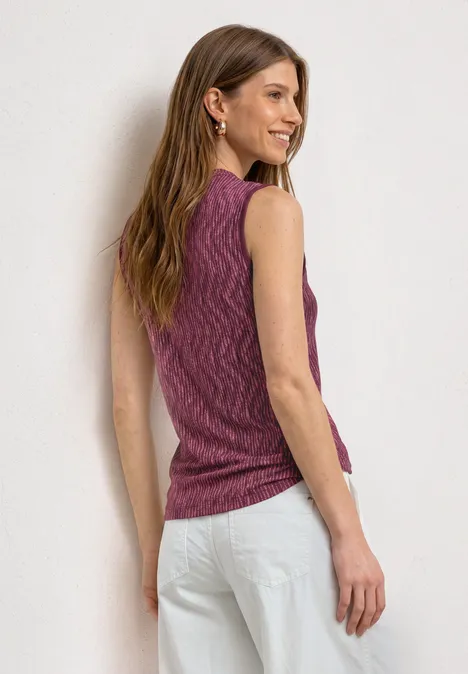 Femme de dos portant un top sans manches rose et un pantalon blanc.