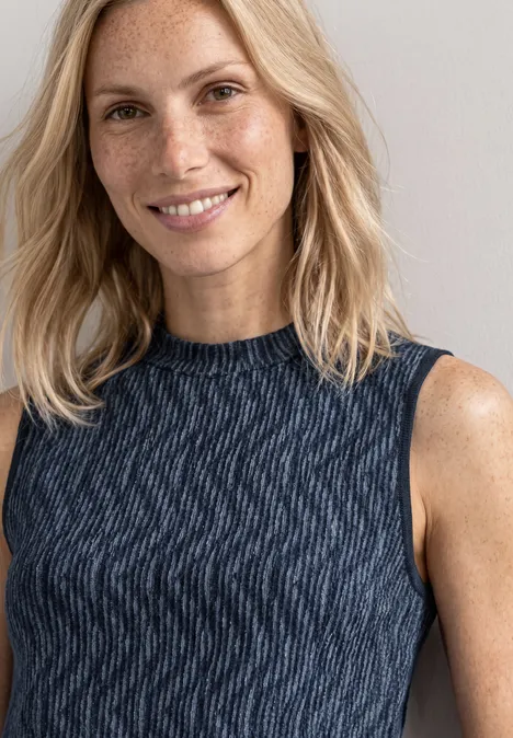 Top mit Turtle Neck und Print ashen blue Porträt einer lächelnden, blondhaarigen Frau mit Sommersprossen in einem dunkelblauen, ärmellosen Top.