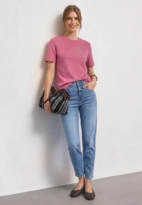 T-Shirt mit Rundhals und Chestprint blush berry Frau in pinkem T-Shirt, blauen Jeans und Loafers, hält gestreifte Tasche vor weißem Hintergrund.