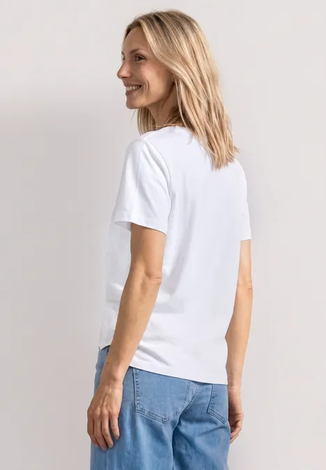 T-Shirt mit Rundhals und Fotoprint White Eine blonde Frau steht seitlich, trägt ein weißes T-Shirt und blaue Jeans.