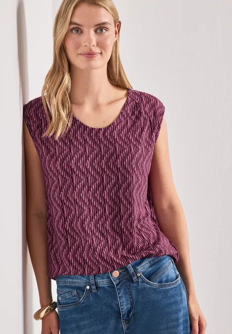 Shirt met afhangende schouders en elastische zoom blush berry Vrouw leunt tegen witte muur, draagt paars patroon top en jeans