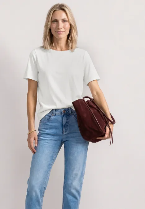 Basic T-Shirt mit Rundhals in Unifarbe off white Frau in weißem T-Shirt und blauen Jeans, lässig mit brauner Lederhandtasche.