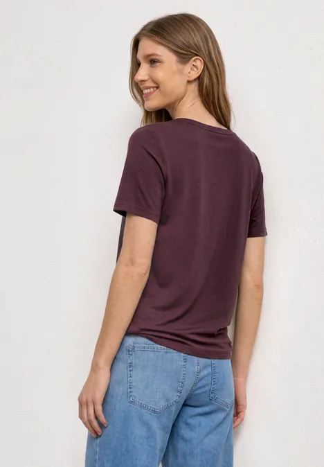 Basic Shirt met ronde hals in Unifarbe rustic rouge Vrouw van achteren in paars t-shirt en blauwe spijkerbroek tegen lichte achtergrond.