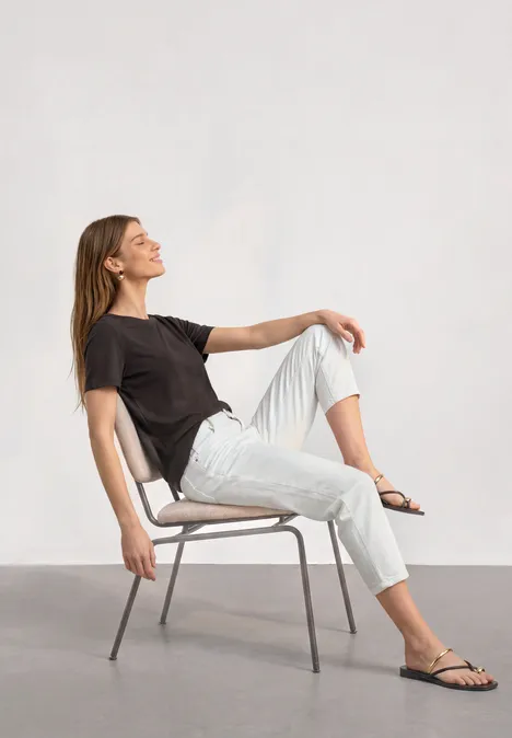 Basic T-Shirt mit Rundhals in Unifarbe black coffee Eine Frau in legerer Kleidung sitzt entspannt auf einem Stuhl, lehnt sich zurück und lächelt.
