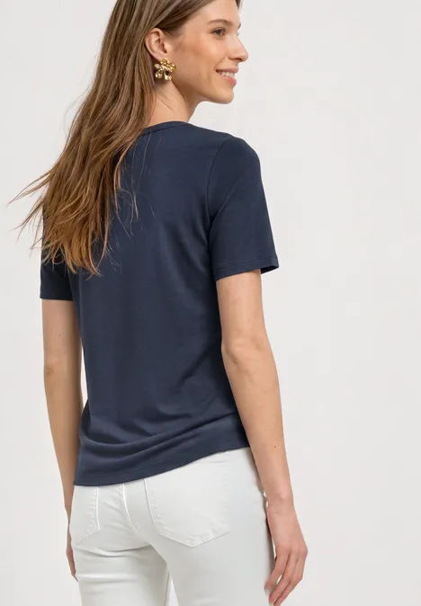 Basic T-Shirt mit Rundhals in Unifarbe darkest blue Eine Frau steht seitlich, trägt ein dunkelblaues T-Shirt und weiße Hose, lächelt.