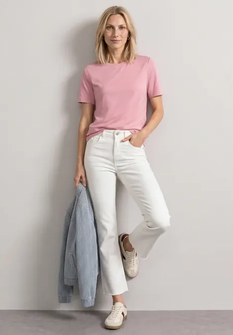 Basic T-Shirt mit Rundhals in Unifarbe vintage blush Frau in rosa T-Shirt und weißen Jeans lehnt lässig an der Wand, hält eine Jeansjacke in der Hand.