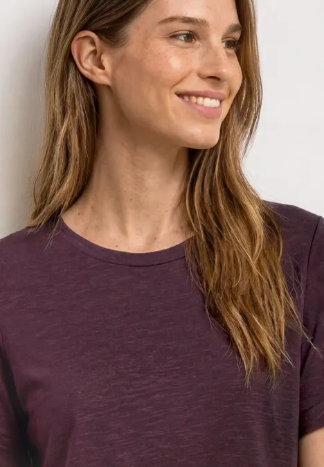 Frau in lila T-Shirt mit langen Haaren, Schultern und Hals sichtbar