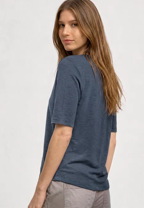 Seitenansicht einer Person mit mittellangen Haaren, grauem T-Shirt und heller Hose.