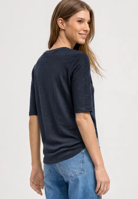 Junge Frau in dunklem T-Shirt und blauer Jeans blickt über die Schulter.