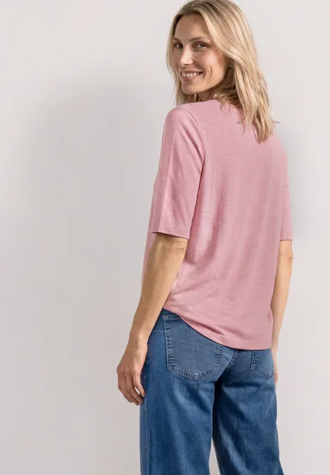 Een persoon staat met de rug naar de camera, draagt een roze shirt en een blauwe broek.