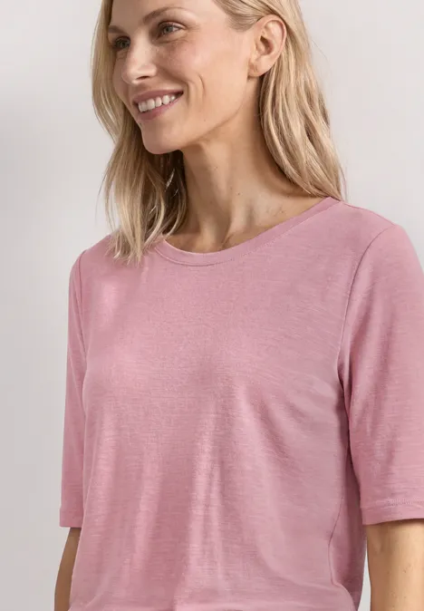 Een vrouw met blond haar draagt een eenvoudig roze T-shirt voor een lichte achtergrond.
