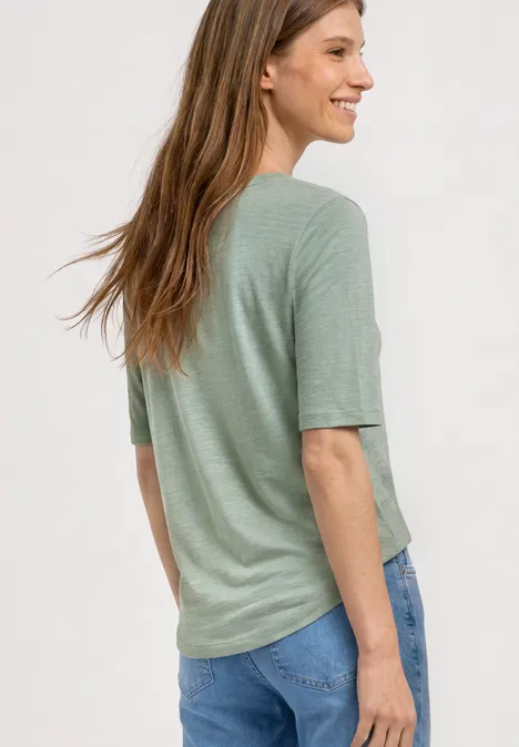 Eine Frau von hinten trägt ein hellgrünes Shirt und blaue Jeans.