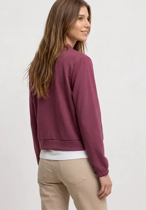 Langarm Jacke im verkürzten Schnitt dark clouded blush Frau in beigen Hosen und weißem T-Shirt, trägt darüber ein kastanienbraunes Sweatshirt, steht seitlich mit Blick zurück.