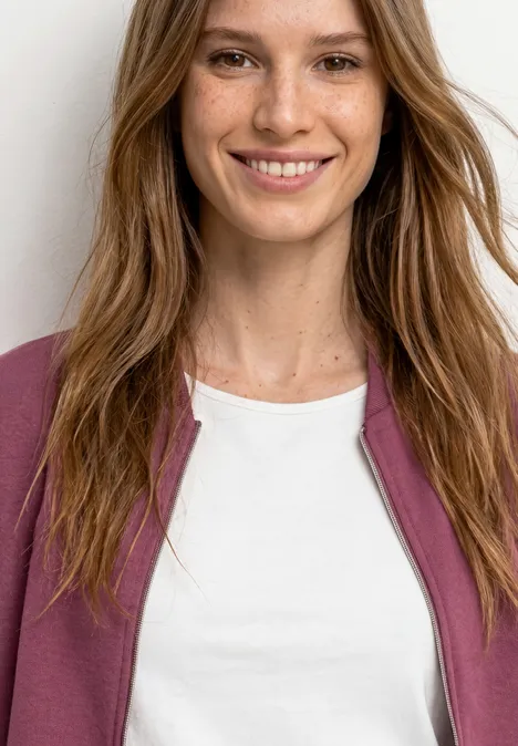 Langarm Jacke im verkürzten Schnitt dark clouded blush Eine lächelnde Frau mit langen braunen Haaren trägt ein weißes T-Shirt und eine rosa Jacke.