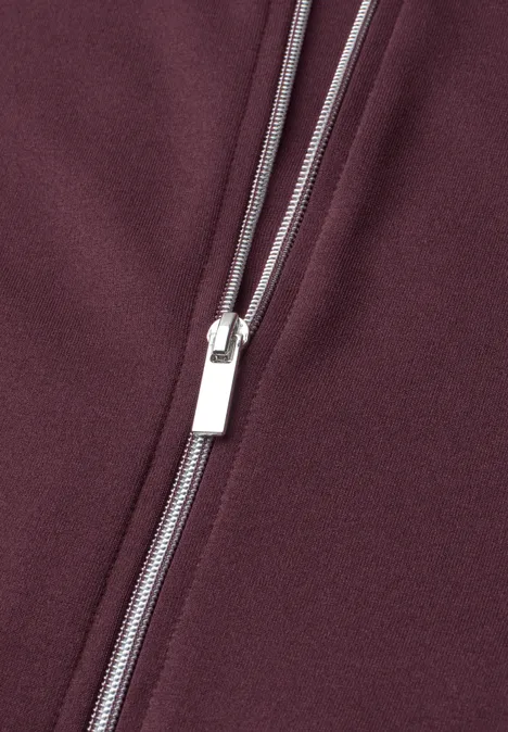 Jas met lange mouwen en een korter model rustic rouge Close-up van een zilverkleurige rits op bordeauxrode stof.