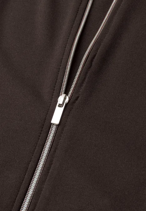 Jas met lange mouwen en een korter model black coffee Close-up van een zilverkleurige rits op donkere stof.
