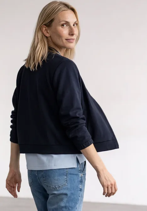 Jas met lange mouwen en een korter model darkest blue Blonde vrouw in zijaanzicht met donkerblauw jasje en jeans, kijkt over haar schouder.