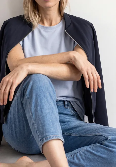 Jas met lange mouwen en een korter model darkest blue Vrouw zit met gekruiste benen, draagt een jeans, licht T-shirt en een blazer los over de schouders.