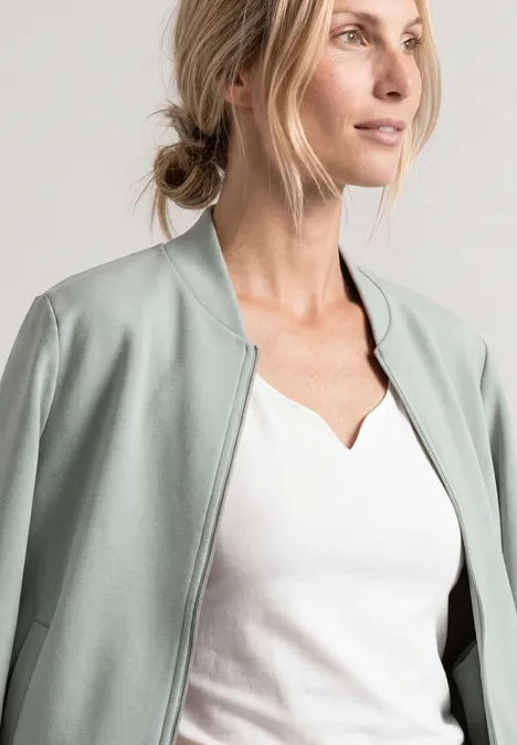 Jas met lange mouwen en een korter model eucalyptus green Blonde vrouw in wit shirt en mintgroen jasje, zijwaarts in de verte kijkend.