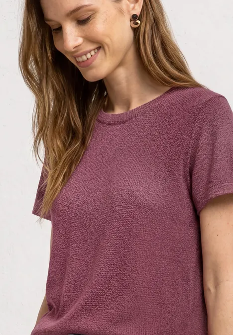 Vrouw met lang haar draagt een losvallend, paars t-shirt met korte mouwen, zachte structuur en gouden creolen.