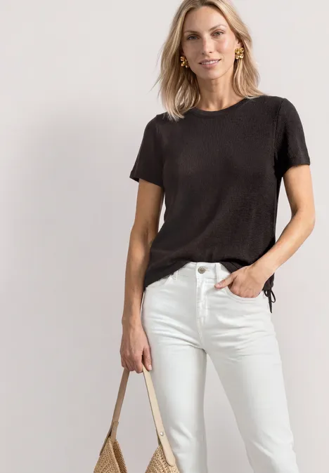 Vrouw in zwart T-shirt en witte spijkerbroek met een beige tas.