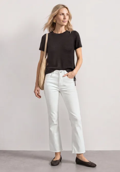 Persoon in casual outfit: zwart t-shirt, witte jeans, zwarte ballerina's en een beige tas.