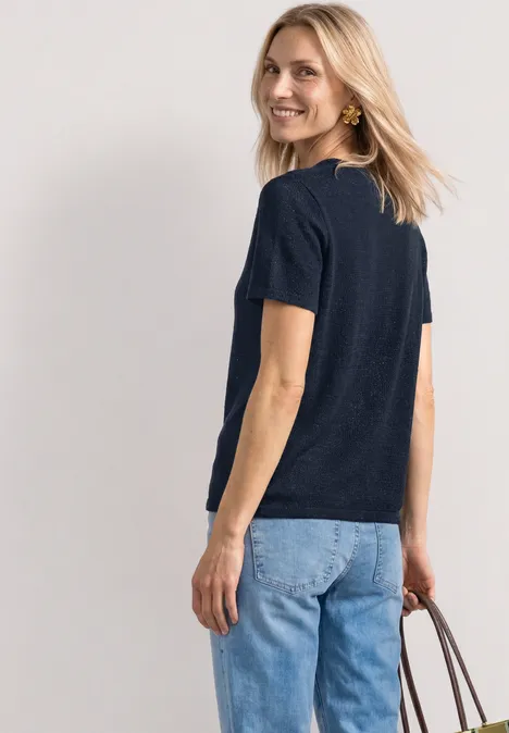 Een vrouw van achteren draagt een donkerblauw shirt, lichte spijkerbroek en houdt een bruine handtas vast.