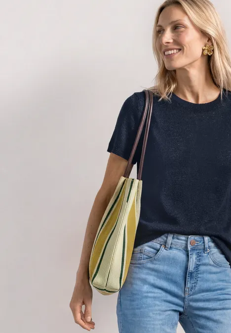 Vrouw in donkerblauw shirt en spijkerbroek met een gestreepte groen-beige schoudertas.
