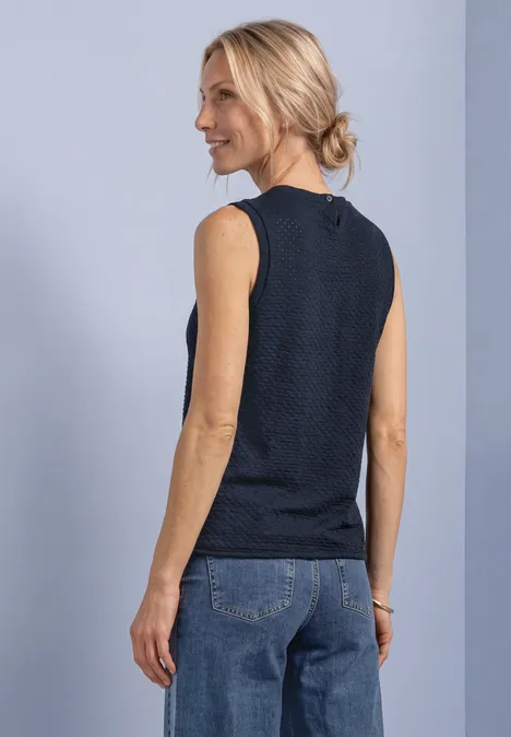 Haut à col en V et patte de boutonnage décorative darkest blue Frau im Profil, sie trägt ein ärmelloses, dunkelblau strukturiertes Top und Jeans vor hellem Hintergrund.