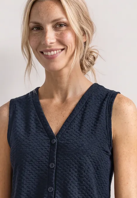 Haut à col en V et patte de boutonnage décorative darkest blue Lächelnde Frau mit blonden Haaren in dunkelblauer, ärmelloser V-Neck-Bluse mit Knöpfen.