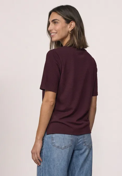 Frau im dunkelroten T-Shirt und blauen Jeans schaut lächelnd über die Schulter.