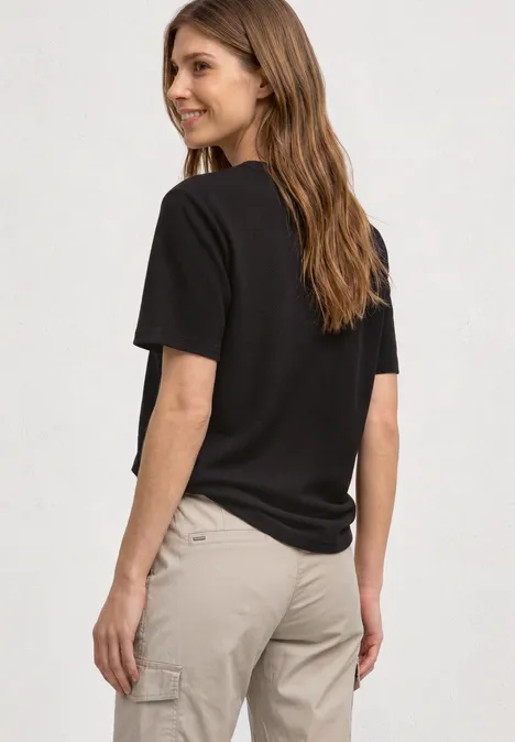T-Shirt mit Rundhals und Struktur black coffee Frau mit schwarzem T-Shirt und beigen Cargohosen, langen braunen Haaren blickt über die Schulter vor hellem Hintergrund.