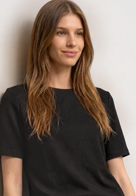 T-Shirt mit Rundhals und Struktur black coffee Eine junge Frau in schwarzem Shirt lehnt entspannt an einer Wand und lächelt leicht.