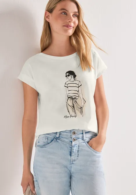 Vrouw draagt wit T-shirt met zwarte lijntekening van zittend figuur en een lichtblauwe jeans