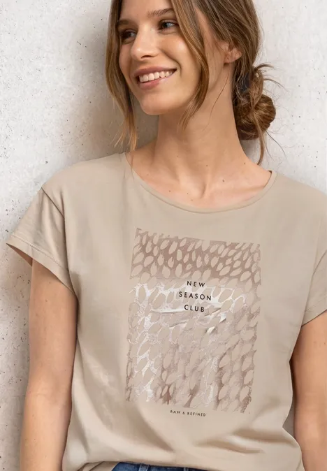 T-Shirt mit Rundhals und Foliendetails clay sand Eine lächelnde Frau in beigem T-Shirt mit abstraktem Print.