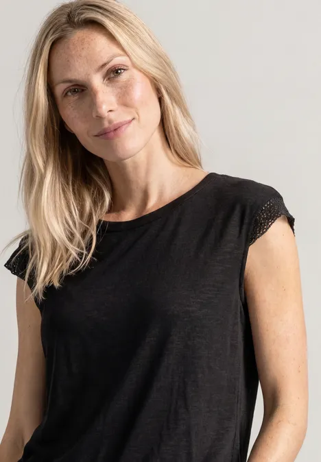 Een glimlachende blonde vrouw draagt een zwart topje en kijkt in de camera.